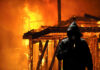 Hooded figure holding lighter in front of fire