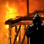 Hooded figure holding lighter in front of fire