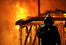 Hooded figure holding lighter in front of fire