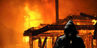 Hooded figure holding lighter in front of fire