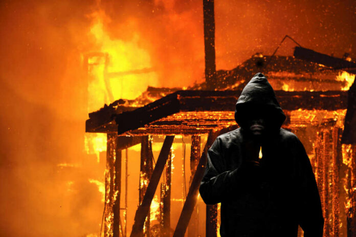 arsonist244348039jpg Hooded figure holding lighter in front of fire
