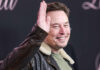 Man smiling while raising his right hand wearing jacket