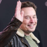 Man smiling while raising his right hand wearing jacket
