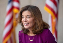 Fact-Check Smackdown Rocks Hochul Smiling woman in a purple dress with flags behind