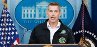 Man speaking at podium with presidential seal and flags