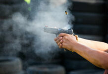 Hands firing a semi-automatic pistol with smoke and ejected casing