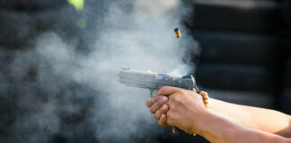 Hands firing a semi-automatic pistol with smoke and ejected casing