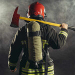 Firefighter holding an axe over their shoulder in a smoky environment