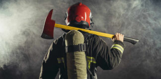 Firefighter holding an axe over their shoulder in a smoky environment