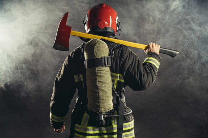 Firefighter holding an axe over their shoulder in a smoky environment