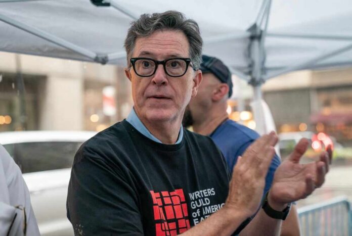 A man in a black t-shirt with a writer's guild logo, clapping at a public event