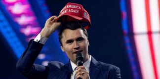 Man in a suit holding a red cap while speaking into a microphone