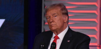 Man in suit at a microphone, red background.