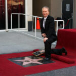 man in a suit kneeling by a Hollywood Walk of Fame star