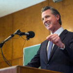 Newsom’s Tax Push Sparks New Backlash Man speaking at podium with microphone