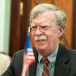 Man with glasses smiling near small American flag