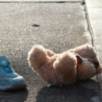 Teddy bear and blue child’s shoe on a sunlit sidewalk