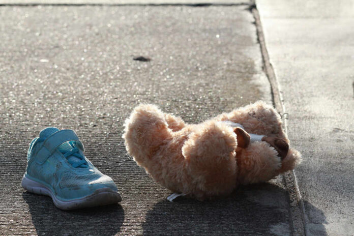 Teddy bear and blue child’s shoe on a sunlit sidewalk