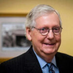 Smiling man in suit with round glasses indoors.