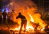 Protester near burning barricade facing riot police at night