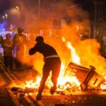 Protester near burning barricade facing riot police at night