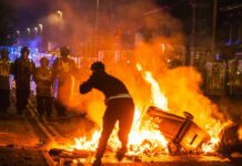 Protester near burning barricade facing riot police at night