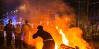 Protester near burning barricade facing riot police at night