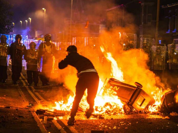 Protester near burning barricade facing riot police at night
