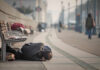 Person sleeping on a city sidewalk beside benches