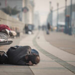 Person sleeping on a city sidewalk beside benches