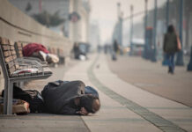 Person sleeping on a city sidewalk beside benches