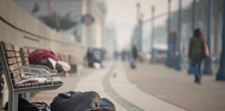 Person sleeping on a city sidewalk beside benches