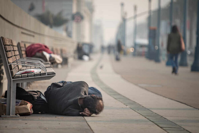 Person sleeping on a city sidewalk beside benches