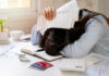 Woman with head on desk amid bills and credit cards