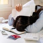 Woman with head on desk amid bills and credit cards