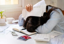 Woman with head on desk amid bills and credit cards