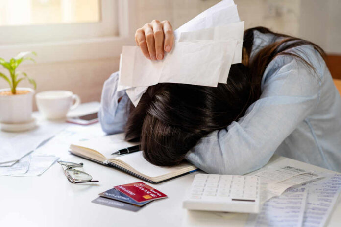Woman with head on desk amid bills and credit cards