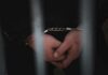Close-up of handcuffed hands behind bars