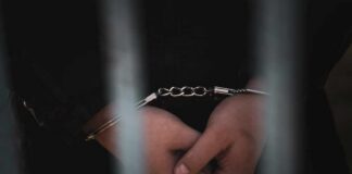 Close-up of handcuffed hands behind bars