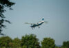 Small airplane flying over green trees and clear sky