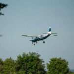 Small airplane flying over green trees and clear sky