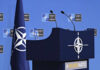 Trump Pushes NATO Toward A New Reality NATO podium with flags and microphones.