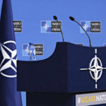 NATO podium with flags and microphones.