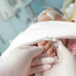 A Toddler’s Symptoms Hid A Deadly Disease Gloved hands holding a baby's hand in a hospital bed