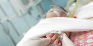 Gloved hands holding a baby's hand in a hospital bed
