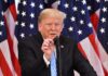 man speaking at a podium with American flags behind him