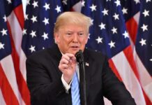 man speaking at a podium with American flags behind him