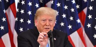 man speaking at a podium with American flags behind him