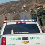 Border Patrol agents gather near fence with patrol trucks