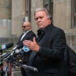 man in black suit speaking at outdoor press conference